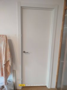 Установлена новая белая дверь с ручкой, аккуратно закреплена в проеме. Смонтированы наличники, обеспечивающие плотное прилегание. Работа завершена, все элементы на месте.