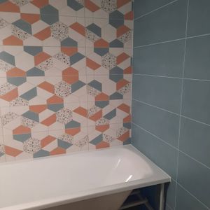 На стенах ванной комнаты уложен керамогранит с геометрическим узором и однотонными плитками. Завершенная работа демонстрирует аккуратное сочетание цветов и ровные швы.