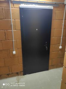 Изображена установленная металлическая дверь в кирпичном проеме. Завершены работы по монтажу, включая фиксацию коробки, регулировку петель, установку замка и проверку функционирования.