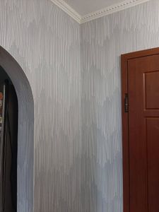 Стены оклеены декоративными полотнами с вертикальным узором, создающим стильный и современный вид. Углы и арки обработаны аккуратно, без видимых стыков и дефектов.
