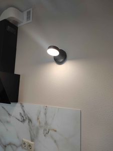 На стене закреплен светильник, подключен к электросети. Проведены работы по установке, обеспечено надежное крепление и функциональность. Свет равномерно освещает пространство.