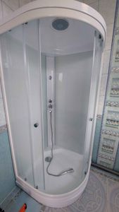 На изображении показана установленная душевая кабина с прозрачными стенками, дверцы закрыты, внутри размещен душевой шланг и лейка. Пол облицован плиткой.