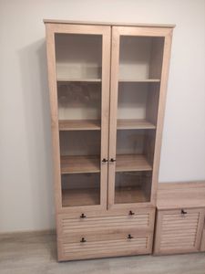 Собран деревянный шкаф с двумя стеклянными дверцами и двумя выдвижными ящиками. Установлены полки, закреплены ручки. Конструкция устойчива и готова к использованию.