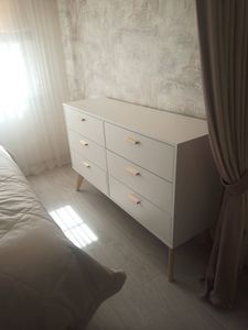Собран белый комод с шестью ящиками, установлен на деревянные ножки. Все элементы аккуратно подогнаны, ручки прикреплены, конструкция устойчива, размещена у стены в светлой комнате.
