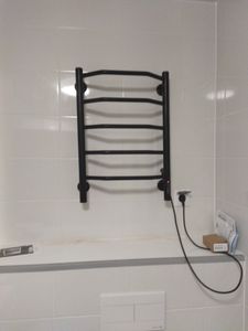Установлен новый черный полотенцесушитель на стену в ванной комнате, подключен к электросети через розетку. Завершены все монтажные работы, устройство готово к использованию.