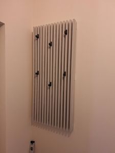 На стене закреплена современная вешалка с вертикальными планками и крючками. Конструкция надежно установлена, обеспечивая функциональность и стильный вид интерьера.