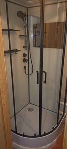 Установлена современная душевая конструкция с прозрачными дверцами и черной рамой. Смонтированы полки, душевой комплект и слив. Завершены все отделочные работы, обеспечена герметичность.