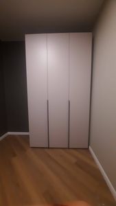 Собран шкаф с тремя дверцами, установлен в углу комнаты. Конструкция выровнена, закреплена, обеспечена устойчивость. Работа выполнена аккуратно, без видимых дефектов.