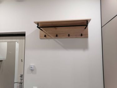 На стене закреплена деревянная полка с металлическими крючками. Установка завершена, конструкция надежно держится, готова к использованию.