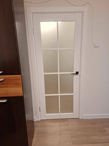 Установлена белая дверь с матовым стеклом, аккуратно вмонтирована в проем, закреплены петли, прикреплена ручка, отрегулированы зазоры, обеспечена плавная работа, завершена отделка наличниками.