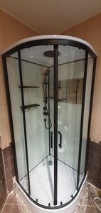 Выполнен монтаж угловой конструкции с прозрачными стенками и черными профилями. Установлены дверцы, поддон и душевой гарнитур. Проведено подключение к водопроводу и герметизация швов.