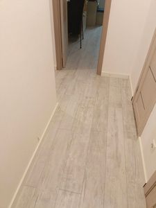 Уложено напольное покрытие из ламината на подготовленное основание в коридоре. Пол ровный, без зазоров, с аккуратными стыками и плинтусами. Светлый оттенок придаёт помещению уют.