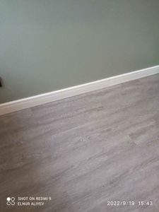 Установлен новый белый плинтус вдоль стены, аккуратно прилегающий к серому полу, создавая завершенный и эстетичный вид интерьера.