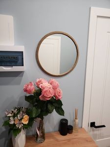Изображение демонстрирует уютный интерьер с круглым зеркалом на стене, рядом с которым стоит стол с вазами, наполненными розами и другими цветами, а также ароматизатором и свечами.
