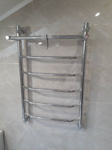 Изображение демонстрирует установленный полотенцесушитель в ванной комнате. Стены облицованы светлой плиткой, создающей аккуратный и современный вид помещения.