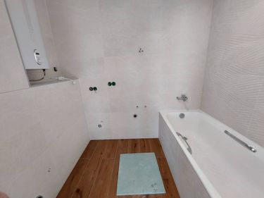 Ванная комната облицована керамогранитом: стены покрыты светлыми плитами, пол оформлен под дерево. Установлена ванна, подключены коммуникации, завершена отделка.