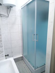 Удалена старая ванна, установлена новая душевая кабина с прозрачными дверцами, подключены водопровод и слив, уложена керамическая плитка на пол и стены, завершены отделочные работы.