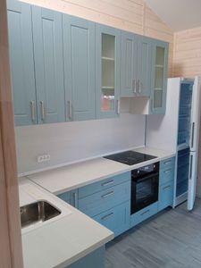 Изображение светлой кухни с голубыми шкафами, встроенной плитой, раковиной и холодильником. Стены отделаны деревом, пол выложен плиткой. Интерьер выглядит современно и аккуратно.