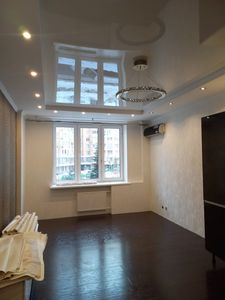 В комнате завершена отделка стен: ровно наклеены обои, создавая аккуратный и стильный интерьер. Светильники и окна подчёркивают обновлённый вид помещения.