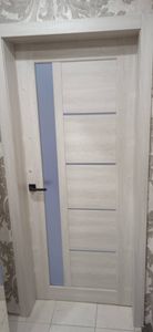 Установлена новая деревянная дверь, закреплена в проеме, добавлены петли, ручка и замок. Полотно ровно выровнено, обеспечена плавная работа, завершена отделка наличниками.