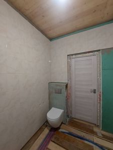 Отделка стен керамическими плитами завершена. Установлен подвесной унитаз. Подготовлены поверхности, уложены элементы ровно, швы аккуратно заделаны. Потолок деревянный.