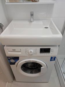 Изображена стиральная машина под раковиной. Устройство подключено к водопроводу и канализации, проверена герметичность соединений, выполнено тестирование работы, установлена на место.