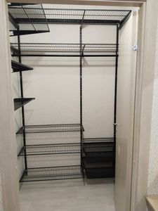 Установлены металлические стеллажи в нише, закреплены на стене. Полки ровно выровнены, обеспечивая надежность и устойчивость конструкции для хранения вещей.