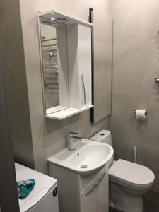 Изображение ванной комнаты с раковиной, зеркальным шкафом, унитазом и полотенцесушителем. На стиральной машине лежит полотенце. Светлые стены и современный дизайн.