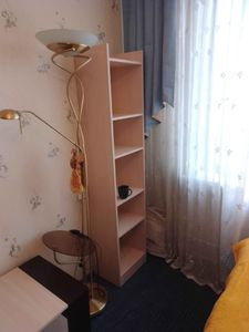 Установлен книжный стеллаж с четырьмя полками в углу комнаты. Элемент мебели аккуратно вписан в интерьер, обеспечивая дополнительное место для хранения.