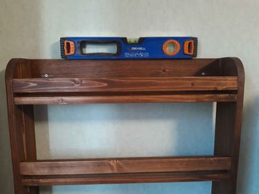 Деревянная полка надежно закреплена на стене. Использован уровень для точного выравнивания. Шурупы вкручены, обеспечивая устойчивость конструкции. Работа завершена аккуратно и качественно.