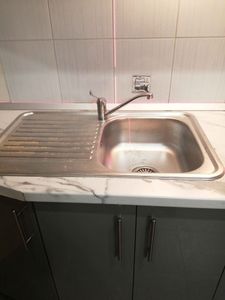 Изображение кухонной мойки с мраморной столешницей, встроенной раковиной и краном на фоне плитки. Видны лазерные линии для выравнивания.