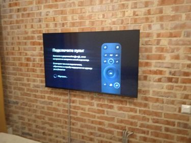 Закреплен кронштейн на кирпичной стене, установлен телевизор, подключены кабели, обеспечена надежная фиксация и аккуратный внешний вид.