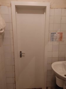 На белой двери установлен замок с ручкой. Проведены работы по вырезанию отверстия, монтажу механизма и фиксации. Дверь закрывается плавно, механизм функционирует исправно.