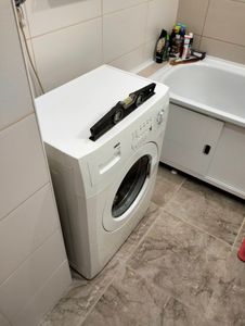 Изображена завершенная установка бытовой техники: подключение к водоснабжению, электричеству, сливу. Уровень проверен, все соединения герметичны, устройство готово к эксплуатации.