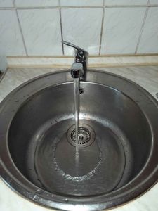 Изображение демонстрирует завершенную работу по замене смесителя на кухонной мойке. Старый кран снят, установлен новый, вода течет плавно, без утечек, поверхность чистая.