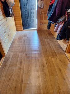 На полу уложено покрытие, имитирующее древесину, без видимых дефектов. Материал ровно распределён, плотно прилегает к основанию, создавая цельную поверхность в помещении.