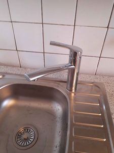 Изображение демонстрирует завершенный демонтаж кухонного гарнитура: удалены шкафы, снята столешница, отсоединены коммуникации, оставлен смеситель и мойка. Стены очищены от крепежей.