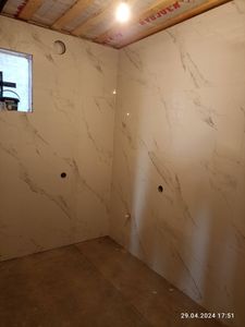 Ванная облицована крупной плиткой с мраморным узором. Стены ровные, швы аккуратные. Установлены отверстия для коммуникаций. Потолок подготовлен, освещение подключено.