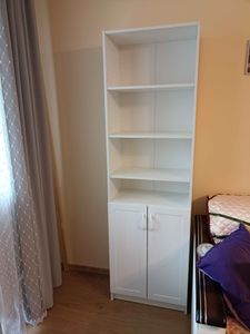 Собрана конструкция с полками и дверцами, установлена в углу комнаты. Стеллаж устойчивый, выполнен из светлого материала, подходит для хранения вещей. Завершённый проект.