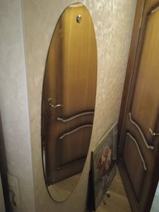 Изображение показывает зеркало в прихожей, отражающее деревянную дверь. На полу стоит картина с цветами.