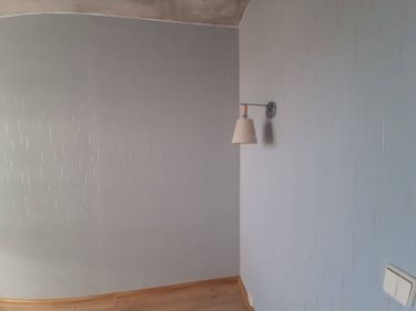 На стену аккуратно нанесены обои с серым узором, без видимых швов и пузырей. Поверхность ровная, без дефектов. Работа завершена, интерьер обновлён, светильник установлен.