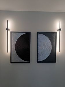 Изображение демонстрирует два абстрактных полотна, закрепленных на стене. Они симметрично расположены между светильниками, создавая гармоничный акцент в интерьере.