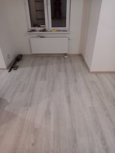 Обновлённое покрытие уложено в комнате, панели ровно подогнаны, плинтусы установлены, стыки аккуратные, поверхность гладкая, цвет светлый, создаёт уютную атмосферу.