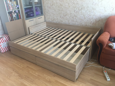 Собрана деревянная конструкция с выдвижными ящиками, уложены ламели, закреплены боковины и спинка. Все элементы соединены, обеспечивая устойчивость и функциональность.