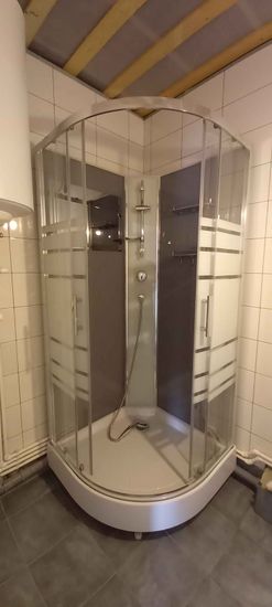 Установлена современная душевая конструкция с прозрачными дверцами и металлическими элементами. Завершена укладка плитки на стенах и полу, подключены водопроводные коммуникации.