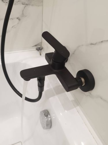 Установлен новый черный смеситель в ванной, подключены трубы, проверена герметичность соединений, вода подается без протечек.