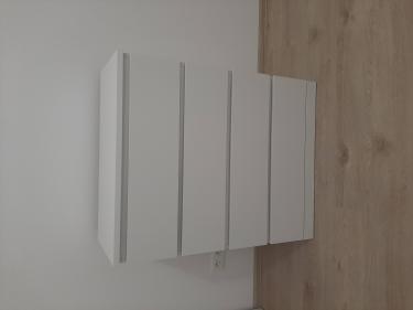 Собран белый комод с четырьмя ящиками, установлен на деревянный пол у стены. Все элементы аккуратно соединены, конструкция устойчива и готова к использованию.