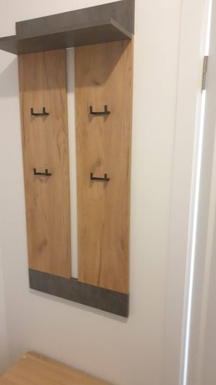 Полка закреплена на стене, обеспечивая устойчивость и надежность. Деревянная конструкция с металлическими крючками установлена ровно, без видимых дефектов.