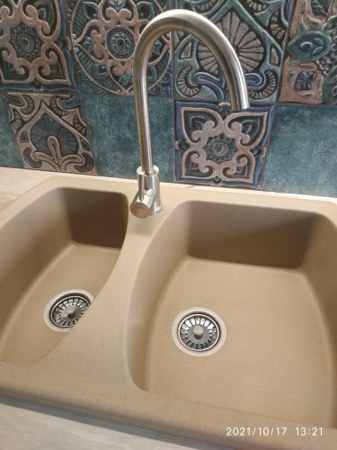 Установлена кухонная мойка с двойной чашей, смеситель подключён, выполнен монтаж столешницы и фартука с узорчатой плиткой. Все элементы гармонично сочетаются, создавая завершённый вид.