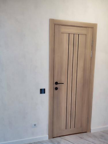 Установлена новая деревянная створка с петлями, ручками и замком. Коробка закреплена, наличники подогнаны, зазоры выровнены. Все элементы тщательно подогнаны для плавного закрывания.